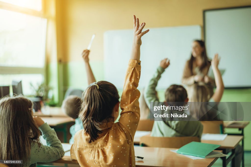 Students Raising Hands While Teacher Asking Them Questions In Classroom ...
