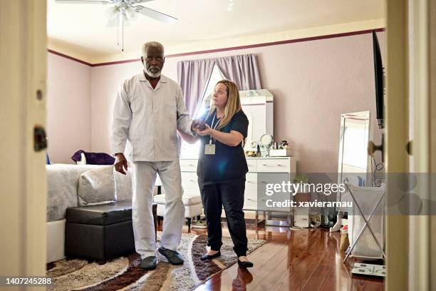 caregiver helping senior man take first steps in the morning - residential care stockfoto's en -beelden