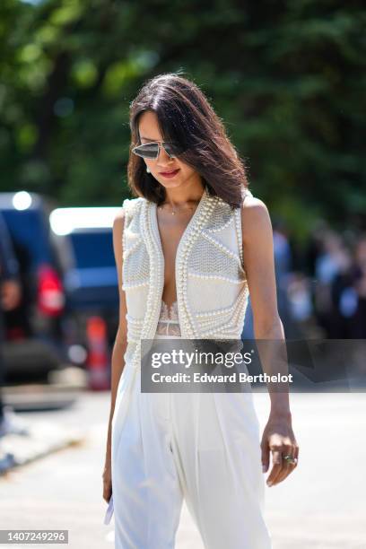 Guest wears sunglasses, gold and pearl pendant earrings, a gold necklace, a white pearls sleeveless / gilet, a white lace V-neck body, white large...