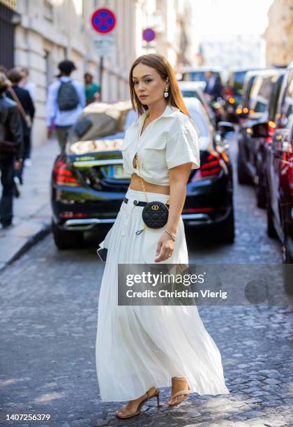 Guest is seen wearing white knotted cropped button shirt, round Dior bag, pleated white high waisted maxi skirt, sandals outside Zuhair Murad during...