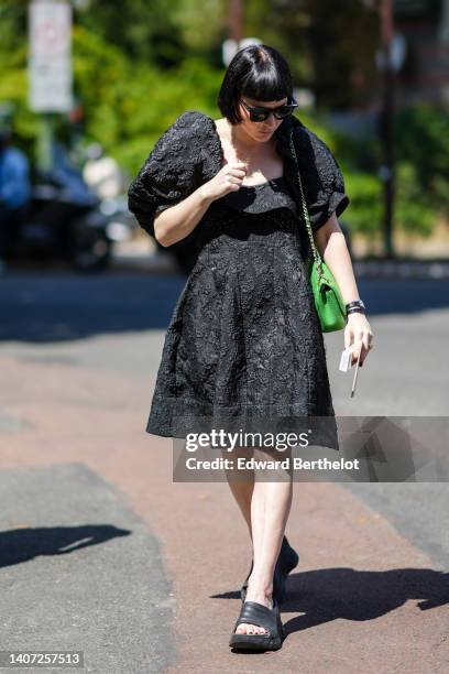 Guest wears black sunglasses, gold necklace, a black embroidered flower square neck / puffy short sleeves knees skirt, a green tweed shoulder bag...