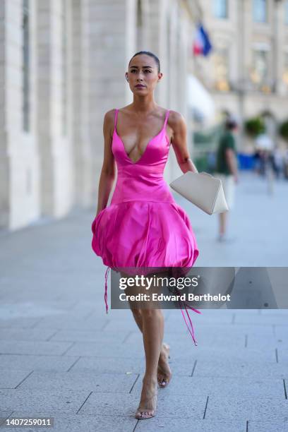 Guest wears rhinestones earrings, a neon pink shiny satin V-neck / puffy short dress, a beige matte leather triangular handbag, transparent strappy...