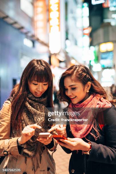 ソーシャルメディアをチェックする東京の街頭で友人たち - 日本　手にもつ　外　仲間 ストックフォトと画像