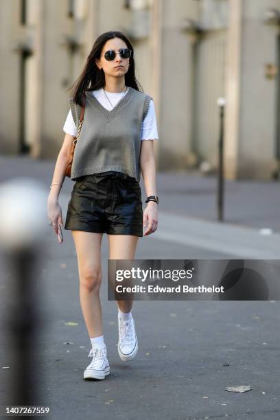 Guest wears black sunglasses, a white t-shirt, a gray V-neck / wool sleeveless pullover, silver pendant necklace, a brown shiny leather shoulder bag,...