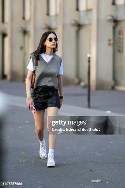 Guest wears black sunglasses, a white t-shirt, a gray V-neck / wool sleeveless pullover, silver pendant necklace, a brown shiny leather shoulder bag,...