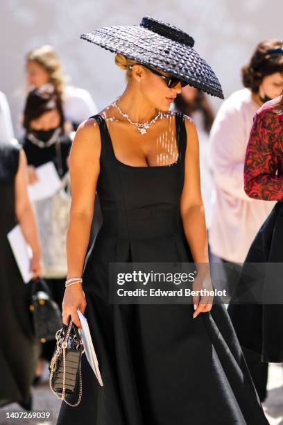 Guest wears a black wicker oversized hat, silver and diamonds flower necklace from Dior, a black square neck / tank-top / long dress, silver...