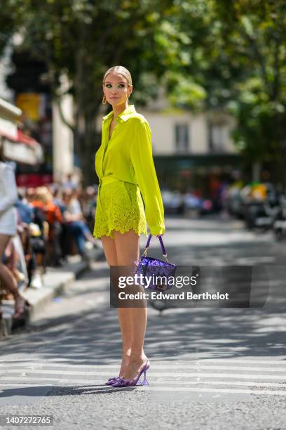 Guest wears gold earrings, a yellow silk shirt, matching yellow lace pattern shorts, a purple shiny sequined handbag from Fendi, a gold large pendant...