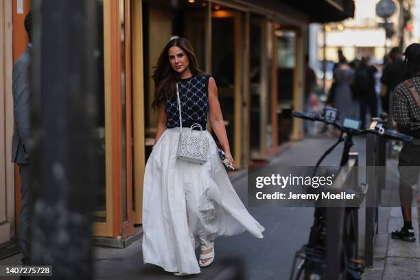 Guest seen wearing gold pendant necklaces, a black bow pattern knit sweater vest, a white oversized pleated long skirt/pants, a white leather hole...