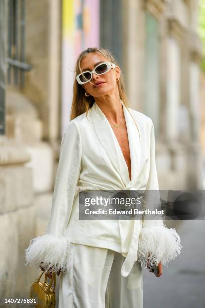 Maja Malnar wears white latte sunglasses, gold earrings, a gold chain pendant necklace, a white latte oversized belted blazer jacket with embroidered...