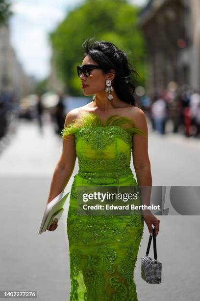 Guest wears black sunglasses, diamonds and crystals pendant earrings, a green feathers / embroidered pearls / shoulder-off tube long dress, a silver...