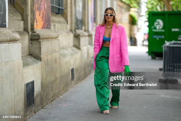 Guest wears white latte sunglasses, a pink linen oversized blazer jacket, gold earrings, a gold large chain necklace, a blue ribbed wool V-neck laces...