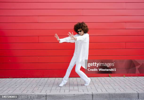 afro woman with sunglasses gesturing on sidewalk in front of red wall - signaling pathways stock-fotos und bilder