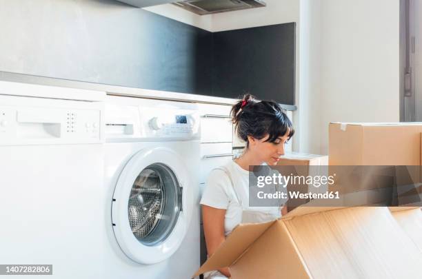 woman looking in cardboard box sitting by washing machine in utility room - utility room stock pictures, royalty-free photos & images