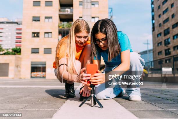 smiling girls adjusting smart phone on tripod - tripod stock-fotos und bilder