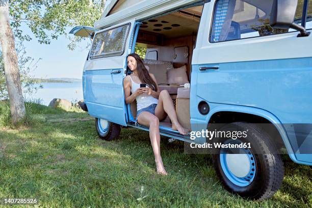 woman with mobile phone day dreaming in motor home by lake - vendeur stockfoto's en -beelden