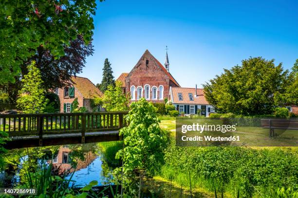 germany, lower saxony, krummhorn, small bridge over standing water withloquard church in background - aurich bildbanksfoton och bilder