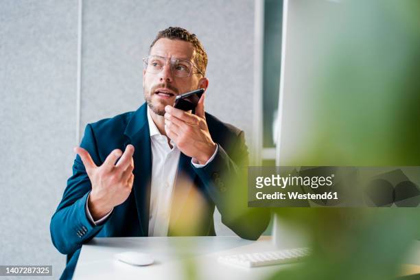 businessman gesturing talking on speaker phone in office - voice command stock pictures, royalty-free photos & images