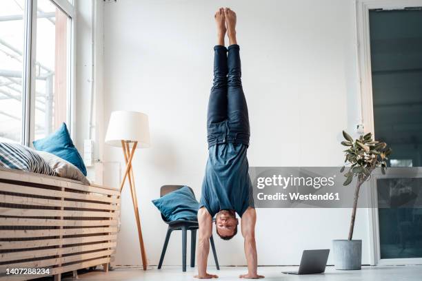 man practicing handstand in front of wall at home - hacer el pino fotografías e imágenes de stock