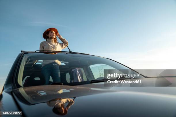 smiling woman wearing hat standing in car through sun roof - sunroof stock pictures, royalty-free photos & images