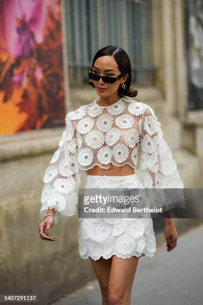 Guest wears black sunglasses, silver earrings, a white transparent with embroidered flower pattern long sleeves / cropped top, a matching white...