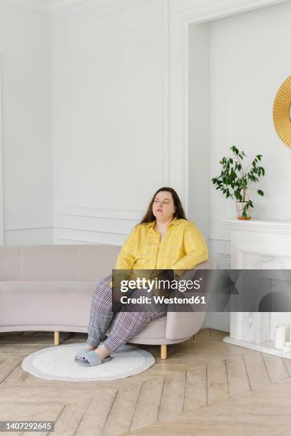 thoughtful woman sitting on sofa at home - nightwear stock pictures, royalty-free photos & images