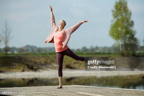 happy woman with arms raised dancing on pier - op een been staan stockfoto's en -beelden