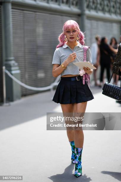 Guest wears pink sunglasses in shape of heart, yellow and blue pendant earrings, gold chain necklaces, a pale gray short sleeves / cropped polo shirt...