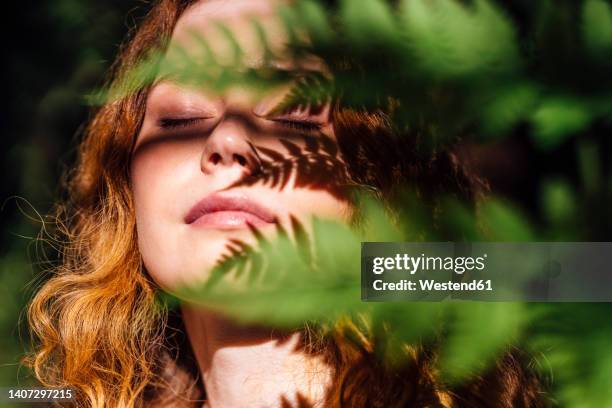 woman with leaf shadow on face enjoying sunlight - einatmen stock-fotos und bilder