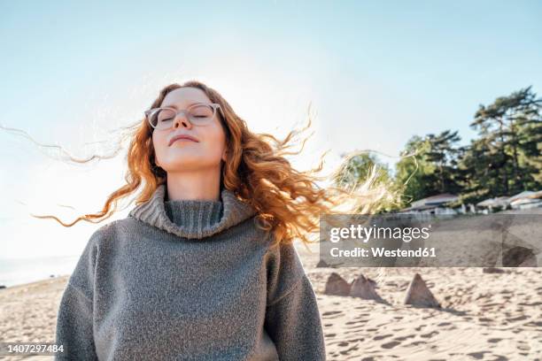 young woman with eyes closed enjoying fresh air at beach - young woman standing against clear sky stock pictures, royalty-free photos & images