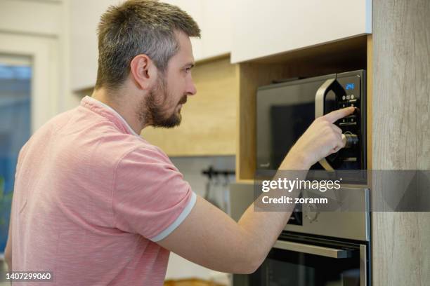 Man Standing By The Oven And Pushing Start Button To Bake Food, Foto de stock