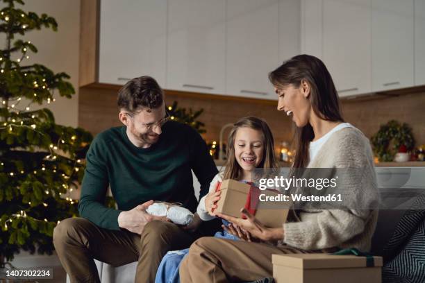 happy parents giving christmas gift to daughter sitting on sofa - child giving gift stock-fotos und bilder