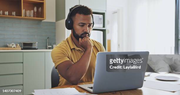 a young businessman using his laptop and thinks about something while sitting and long hours of work from home and wearing a headset too in a serious mood and trying to resolve the problem - long table stockfoto's en -beelden