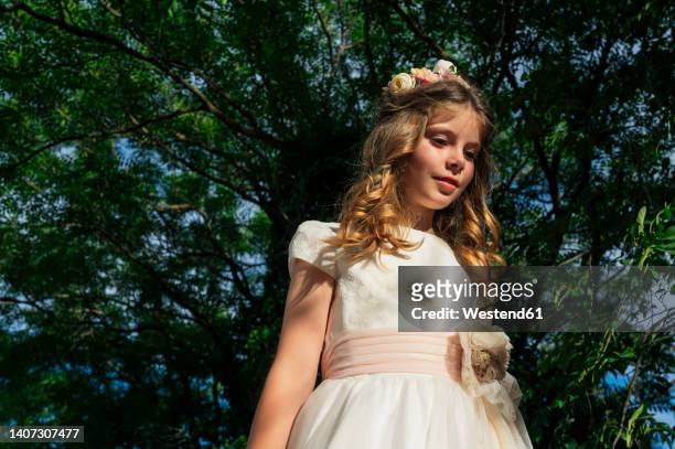 girl wearing communion dress standing under tree - communion fotografías e imágenes de stock