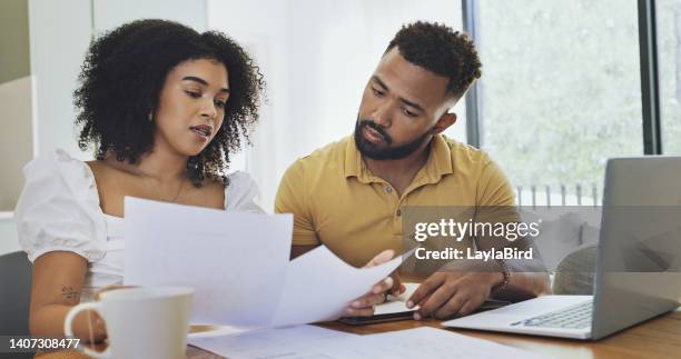 couple reading documents and paying bills using a laptop at home. husband and wife planning their budget and finances. man and woman working on their savings. girlfriend and boyfriend doing taxes - belastingen stockfoto's en -beelden