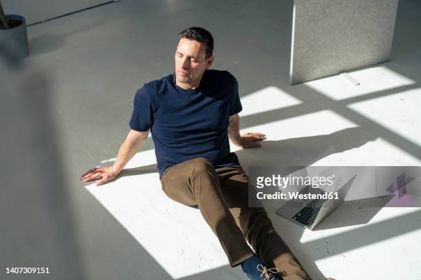 businessman with laptop sitting on floor in sunlight at office - connected mindfulness work stock pictures, royalty-free photos & images