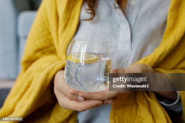 hands of woman holding sparkling water with lemon slice in glass - sparkling water imagens e fotografias de stock