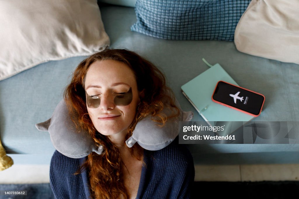 Redhead woman leaning head on sofa with smart phone on airplane mode in living room at home