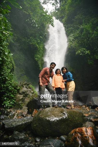 family posing for a photograph while enjoying at a majestic waterfall - indian family vacation stock pictures, royalty-free photos & images
