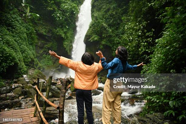 mother and daughter enjoying at a majestic waterfall - indian family vacation stock pictures, royalty-free photos & images