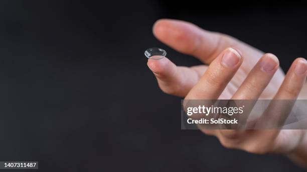 close-up of hand holding contact lens against black background - lente de contacto imagens e fotografias de stock