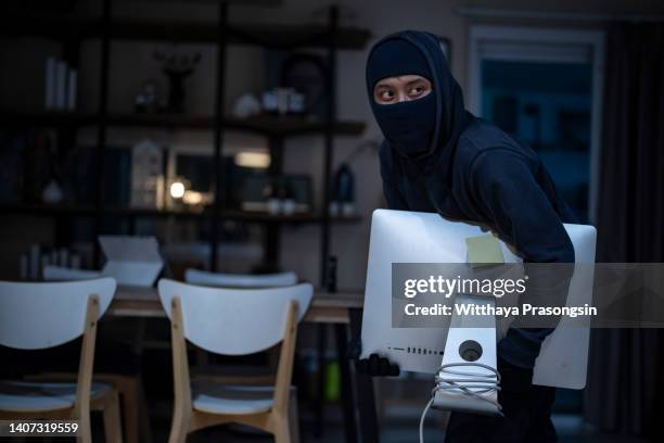 man, criminal dressed all in black, carrying computer that he stole in house. - haus einbruch stock-fotos und bilder