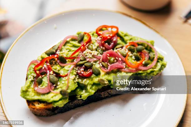 close-up of avocado toast with chilli pepper, onion and pumpkin seeds - raw food diet fotografías e imágenes de stock