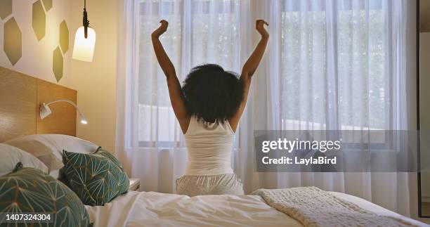 woman stretching arms to wake up and start a good morning on a bright new day from the back at home. one female with curly afro hair getting out of bed and feeling refreshed after some peaceful sleep - black woman hair back stock pictures, royalty-free photos & images
