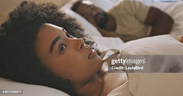 worried black woman laying in bed with insomnia looking anxious and concerned, having infidelity and relationship issues. man sleeping while his wife lays awake at night feeling depressed or troubled - inconveniência imagens e fotografias de stock