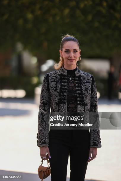 Chiara Ferragni wears gold earrings, a gold pendant necklace, a black lace print pattern high neck t-shirt, a black with embroidered white pattern...