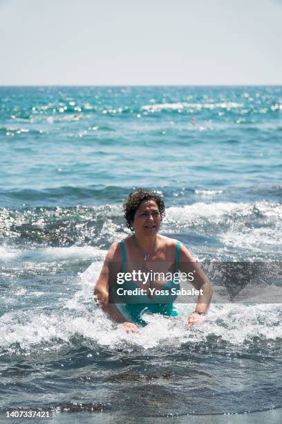 mature woman with curly hair sitting by the seashore - voluptuous mature women foto e immagini stock