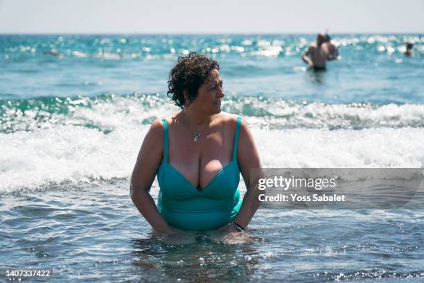 mature woman with curly hair sitting by the seashore - voluptuous mature women foto e immagini stock