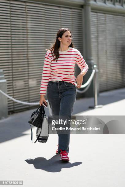 Guest wears gold earrings, a gold pendant necklace, a white latte and red striped print pattern long sleeves t-shirt, gray denim large jeans pants, a...