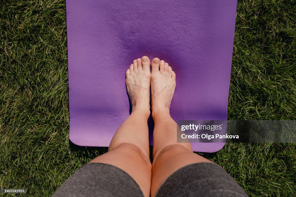 Human feet are standing on a yoga mat on the lawn close-up
