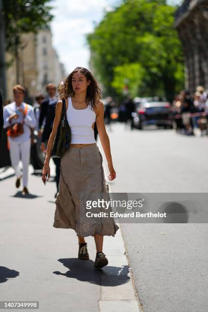 Guest wears a white cut-out waist tank-top, a black shiny leather shoulder bag, a beige ruffled midi skirt, black shiny leather sneakers , outside...